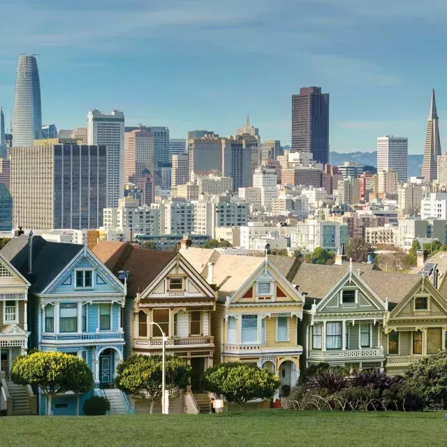 Picknicker sitzen im Gras im Alamo Square Park mit den Painted Ladies und der Skyline von San Francisco im Hintergrund.